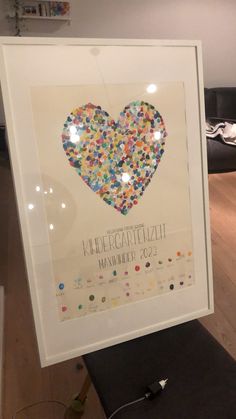 a heart made out of confetti is displayed in a white frame on the floor