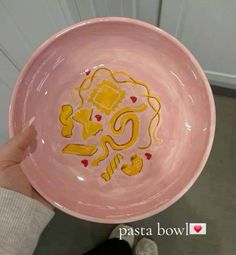 a person holding a pink bowl with yellow designs on the side and red hearts in the middle