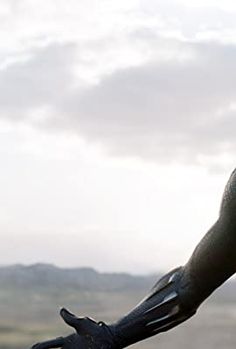 a man wearing a black mask and gloves on top of a hill with mountains in the background