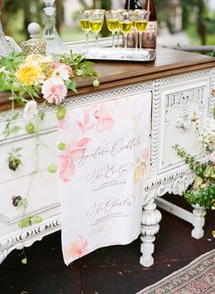 an old dresser with flowers and wine glasses on it is decorated for a wedding reception