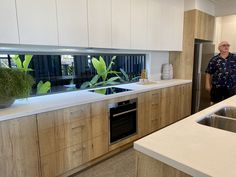 a man standing in a kitchen next to an oven and sink with plants on the counter