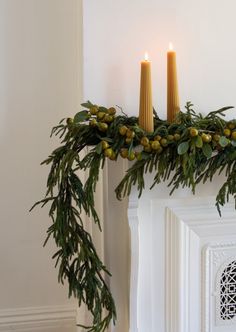 two candles sitting on top of a mantel covered in greenery next to a fireplace