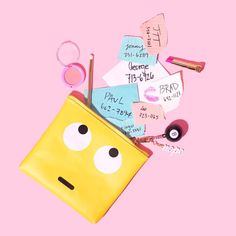 a yellow purse with eyes, lipstick and other items on it's pink background