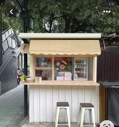 two stools are sitting at the counter in front of a food stand with an awning over it