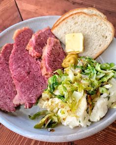 a white plate topped with meat, bread and coleslaw on top of a wooden table