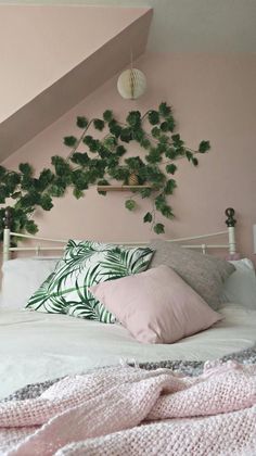 a white bed topped with pillows next to a pink wall and green plants on the headboard