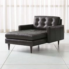 a black leather chair sitting on top of a white tile floor next to a window