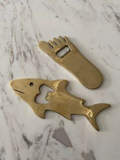 two gold fish shaped bottle openers sitting on top of a marble counter