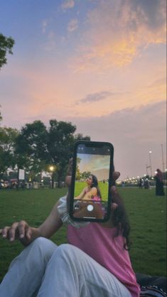 a person holding up a cell phone to take a photo in the park at sunset