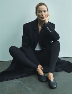 a woman sitting on the ground with her legs crossed, wearing black pants and a blazer