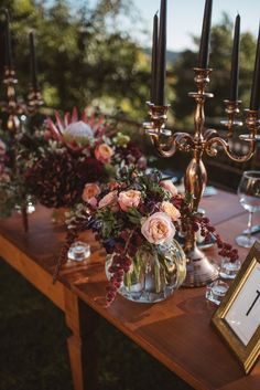 an arrangement of flowers and candles on a table with wine glasses, framed photo frame