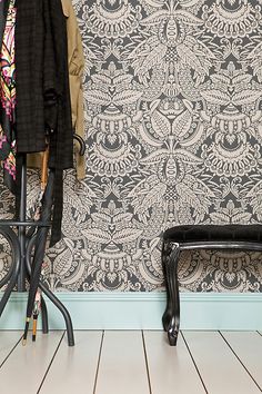 a chair and coat rack in front of a wall with an ornate pattern on it