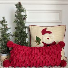 a red knitted pillow sitting next to a christmas tree