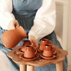 a person sitting on a chair with three cups and saucers in front of them