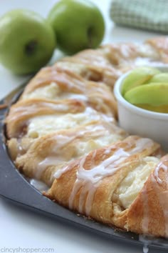 an apple pie with white icing and some green apples on the table next to it