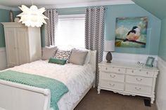 a bed room with a neatly made bed next to a dresser and a painting on the wall