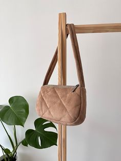 a brown purse hanging from a wooden rack next to a potted plant and white wall