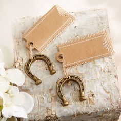 two pairs of earrings sitting on top of a piece of wood next to white flowers