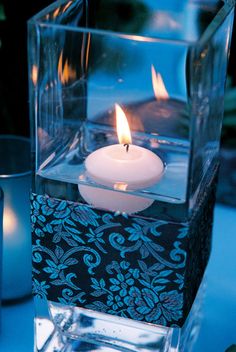 a lit candle sitting inside of a glass container on top of a blue table cloth