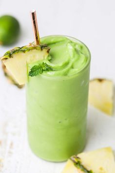 a green smoothie is garnished with mint and topped with a slice of pineapple