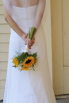 a woman in a white dress holding a bouquet of sunflowers on her wedding day