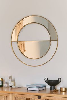 a round mirror on the wall above a wooden cabinet with books and other items sitting on it