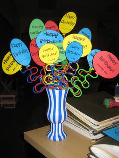 a vase filled with lots of balloons on top of a wooden table next to books