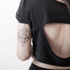 the back of a woman's shirt with a lotus tattoo on her left shoulder