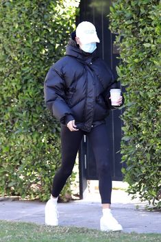 a woman in a black jacket and leggings is walking down the sidewalk with a cup of coffee