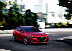 a red car driving down the road in front of tall buildings