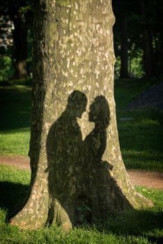 the shadow of two people standing in front of a tree with their arms around each other