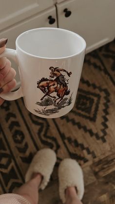 a person holding a coffee mug with a horse design on it, while standing in front of a dresser