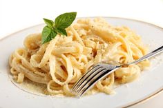 a plate of pasta with basil leaves on top and a fork in the bowl next to it