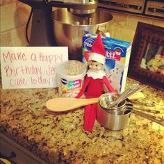 an elf is sitting on the kitchen counter next to some baking supplies and a sign that says make a happy birthday cake today