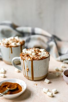 two mugs filled with hot chocolate and marshmallows on top of a table