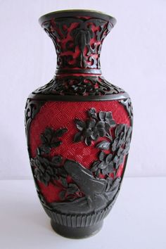 a red and black vase sitting on top of a white table