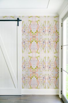 an open white door in front of a wallpapered room with pink and green designs