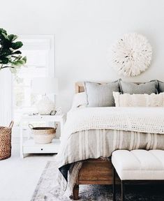 a bedroom with a bed, ottoman and plant in the corner on the wall above it