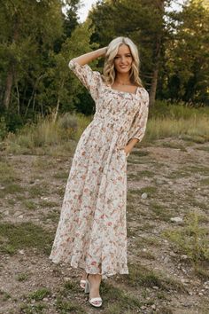 a woman standing in the grass wearing a white floral dress with long sleeves and an open shoulder