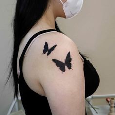 a woman wearing a face mask with two black butterflies on her shoulder and behind her ear