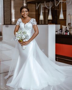 a woman in a white wedding dress holding a bouquet and posing for the camera with her hands on her hips