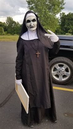 a man dressed in a nun costume standing next to a black truck with a cross on it