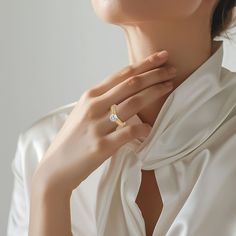 a woman wearing a white shirt with a gold ring on her left hand and a diamond in the middle