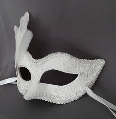 Handmade Venetian style masquerade mask in white. Eye details and edges are outlined with braided trim, front surface is partially covered with pearly off white lace. Decorated with metal rosette and feathers. Back surface is also covered with fabric for comfort. Your order will be delivered with online tracking by UPS or FedEx. Ribbons are added both sides to tie. Base mask is made of paper mache. Standard size fits most (for women). This classical Venetian mask is perfect for any costume or Ha Elegant White Masquerade Mask For Carnival, Elegant White Masquerade Mask For Mardi Gras, White Formal Masquerade Mask For Carnival, White Masquerade Masks And Prosthetics For Mardi Gras, White Masquerade Mask For Halloween, White Masks And Prosthetics For Mardi Gras Masquerade, White Mardi Gras Masquerade Masks And Prosthetics, White Eye Mask For Costume Party, White Venetian Masks And Prosthetics For Theater