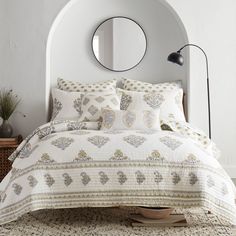 a bed with white and gold comforter in a bedroom next to a round mirror