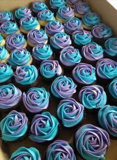 a box filled with blue and purple cupcakes sitting on top of a table