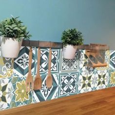 three potted plants and wooden spoons are hanging on a wall with decorative tiles