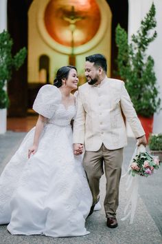 a bride and groom walking together in front of a church door with the bride's bouquet in her hand