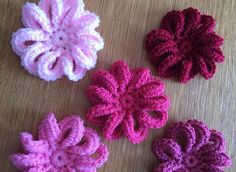 four crocheted flowers sitting on top of a wooden table