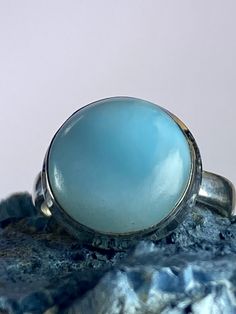 An exceptionally majestic Natural Dominican Larimar and 925 silver ring. This stone is a good size and is of a tranquil, blue coral colour Larimar cabochon set in a fine detailed silver setting. This decorate setting adds complexity and flair to the piece.  Larimar is the embodiment of the tranquil Sea and Sky energies. Its soft, soothing blues and calming turquoise is streaked with white patterns that resemble sunlight dancing beneath Caribbean waters. It brings the ancient wisdom of Atlantis a Blue Round Gemstone Cabochons, Elegant Blue Larimar Turquoise Ring, Blue Larimar Round Rings, Blue Larimar Opal Ring, Blue Cabochon Opal Ring, Blue Opal Oval Cabochon Ring In Sterling Silver, Blue Oval Cabochon Opal Ring In Sterling Silver, Blue Round Cabochons For Anniversary, Blue Larimar Cabochon Rings